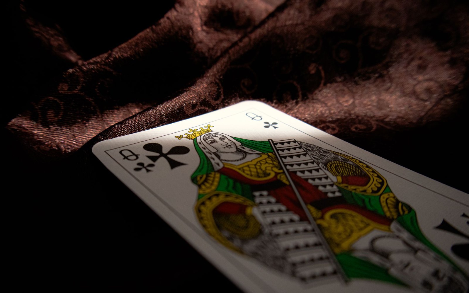 A deck of tarot cards held in a hand, spine toward camera, the gilt edge catching a raking sidelight against a dark cloth background