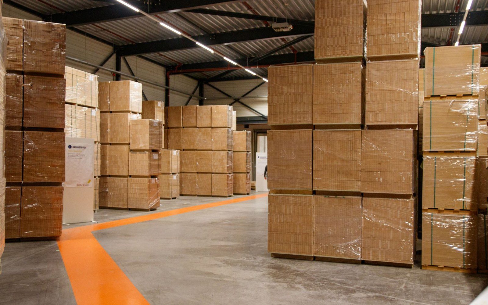 Stacks of shrink-wrapped cardboard boxes on pallets fill a warehouse aisle