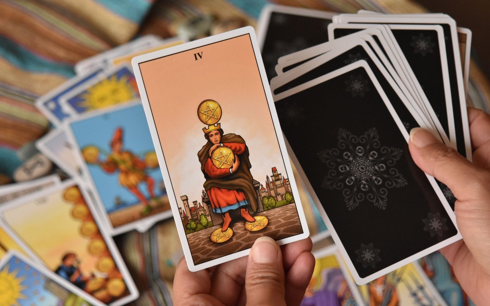 Hands hold a four of pentacles tarot card beside a face-down deck over scattered cards