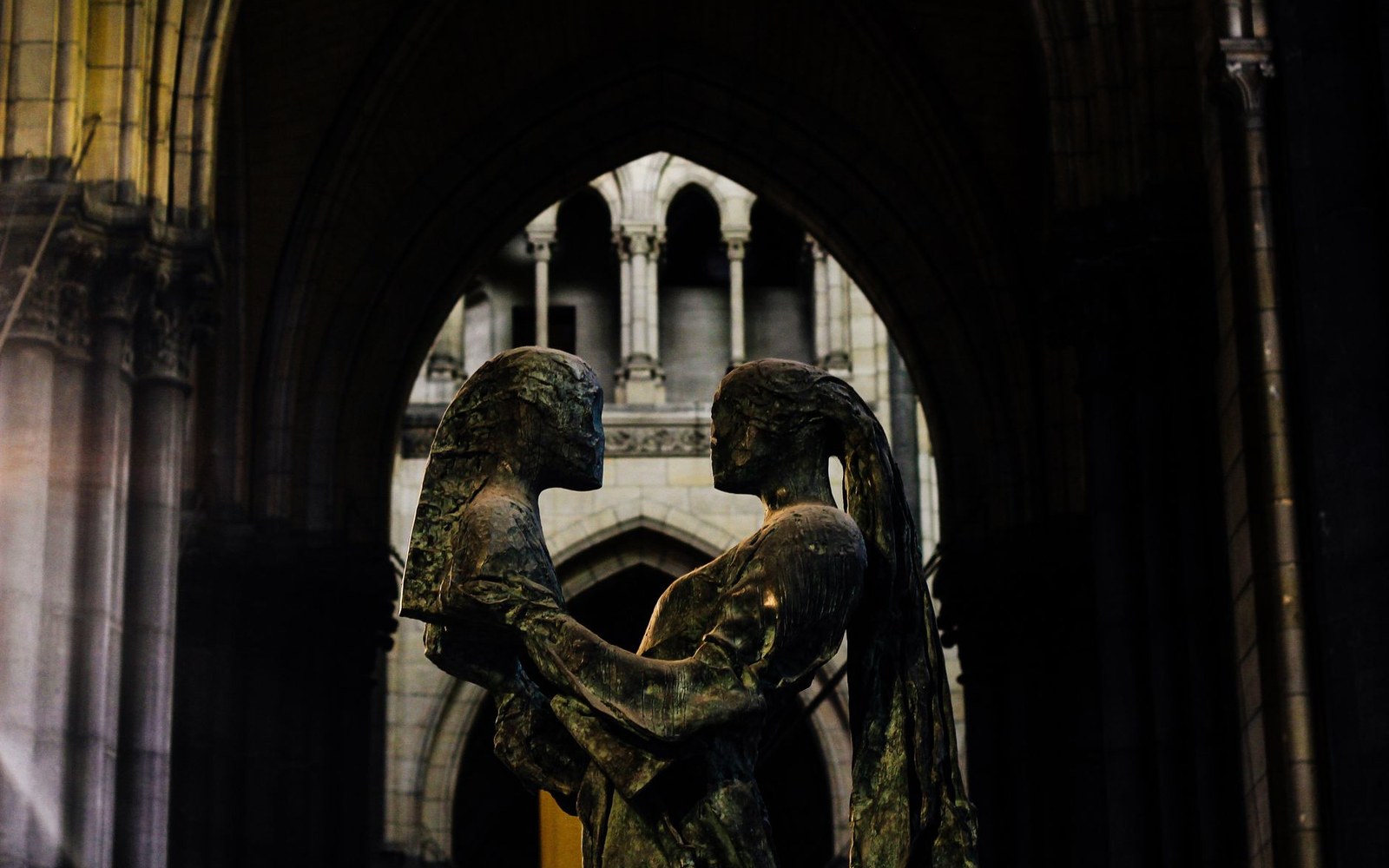 Bronze statue of two embracing figures framed by a stone archway inside a cathedral