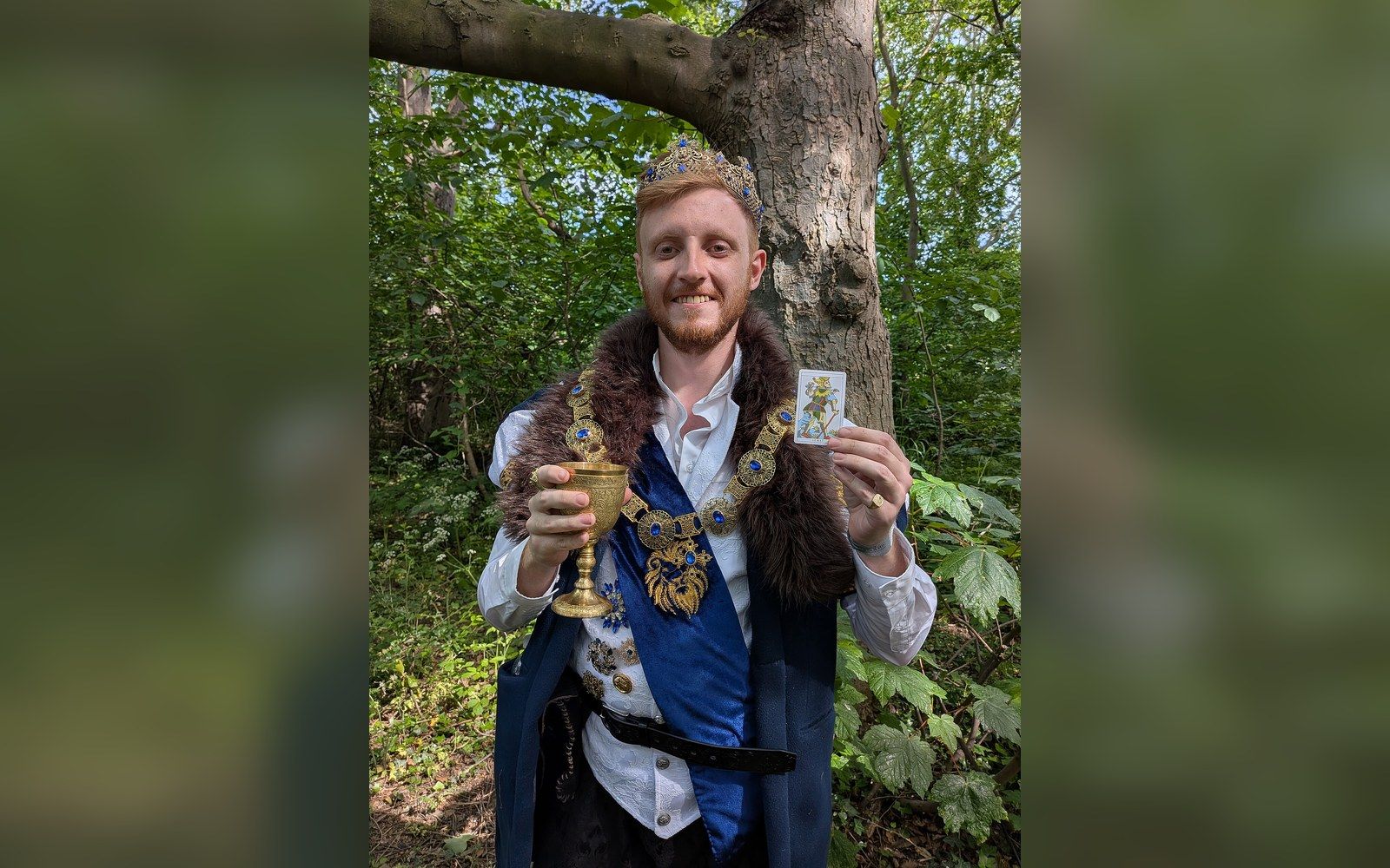 Man in royal costume with crown holds a golden chalice and The Fool tarot card