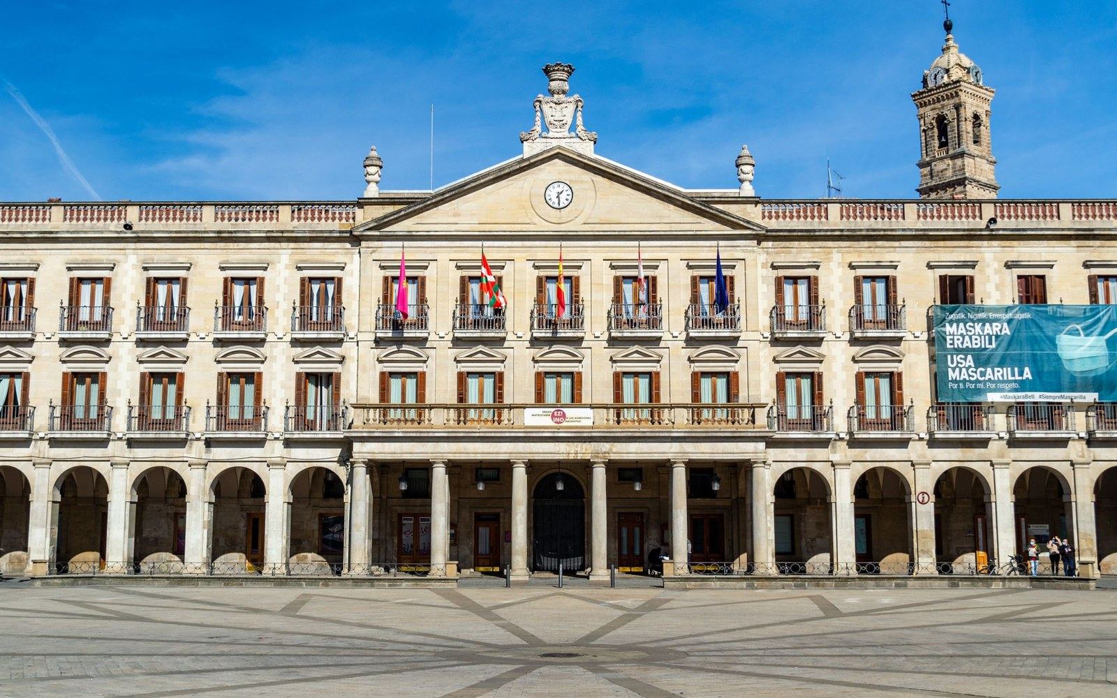 Arcaded facade of Vitoria-Gasteiz's town hall with flags and a clock tower