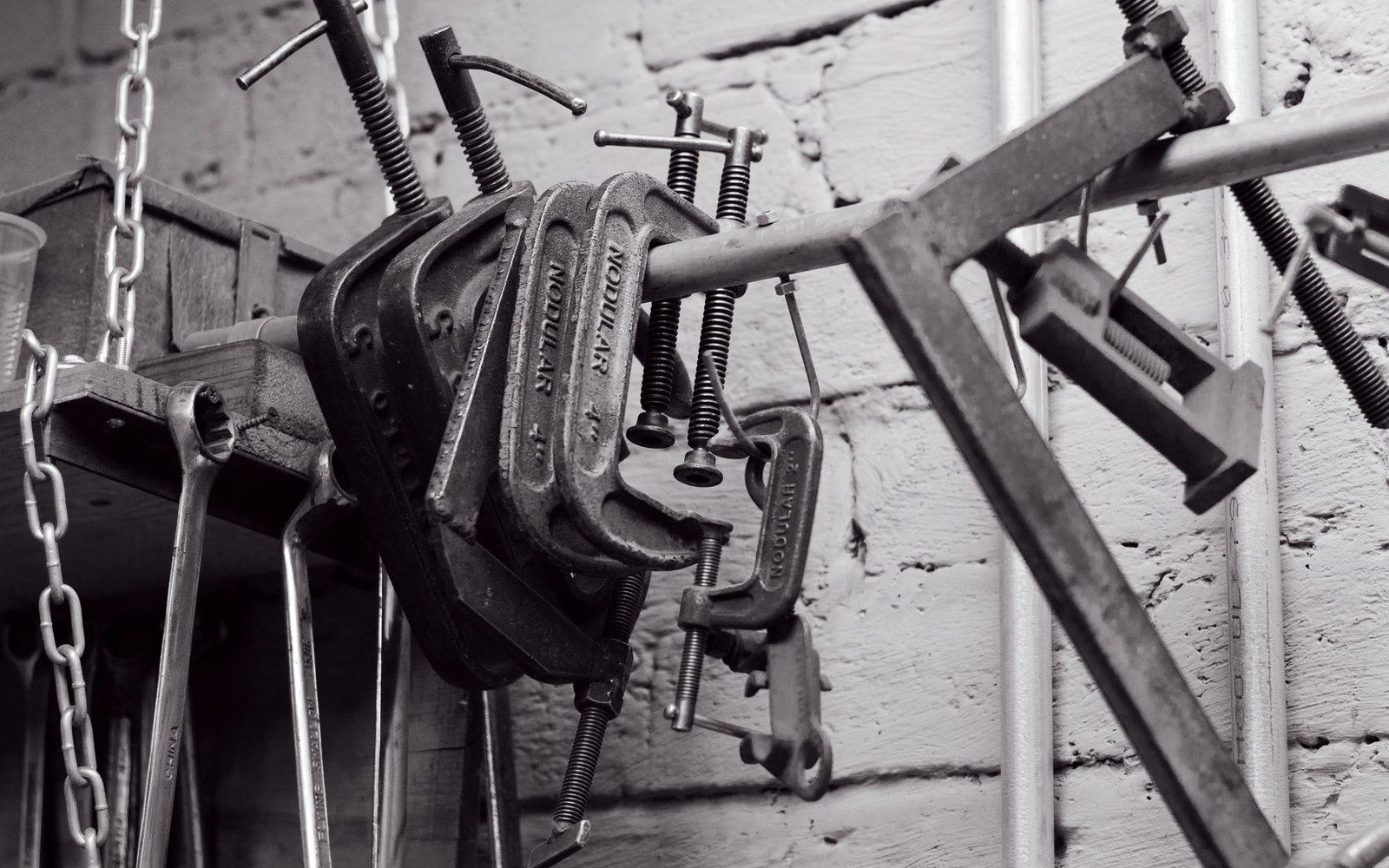 Metal g-clamps hang on a rack against a whitewashed brick workshop wall