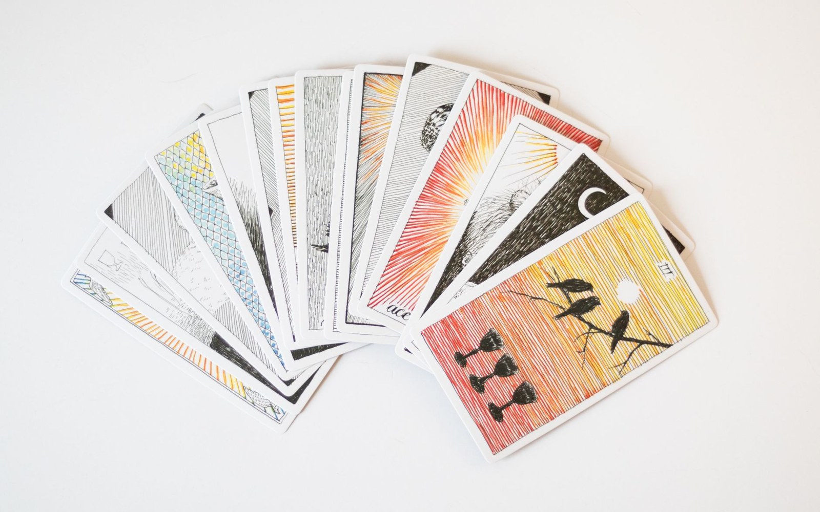 Hand-drawn tarot cards fanned out, featuring line-art suns, moons, birds and geometric patterns