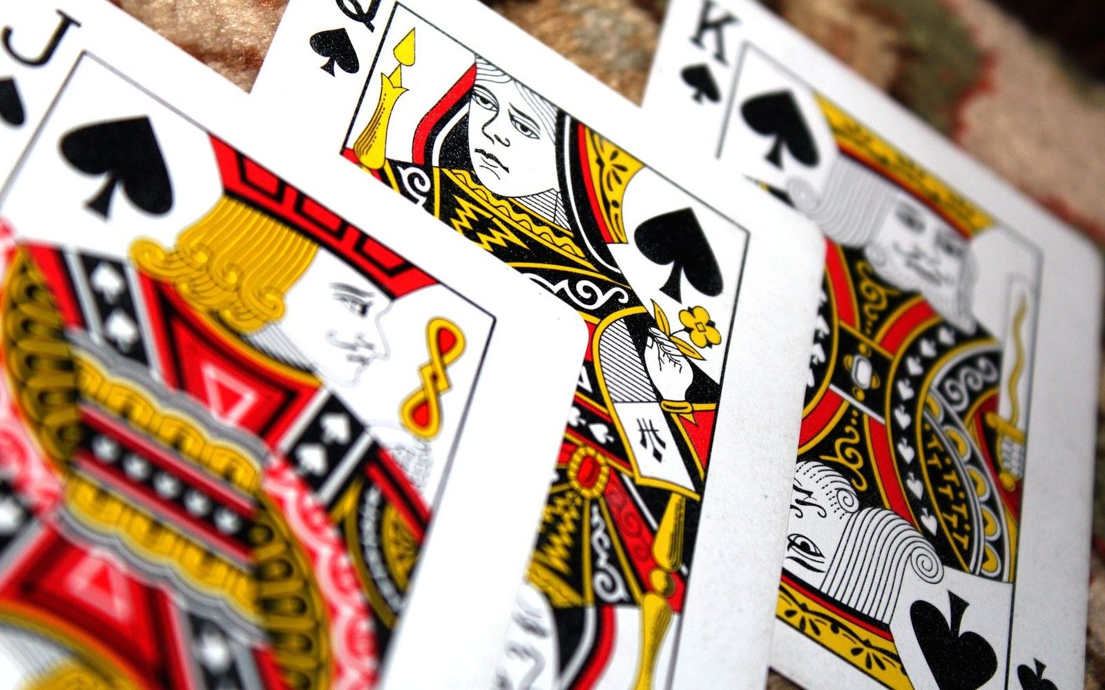 Jack, queen and king of spades playing cards fanned out on a stone surface