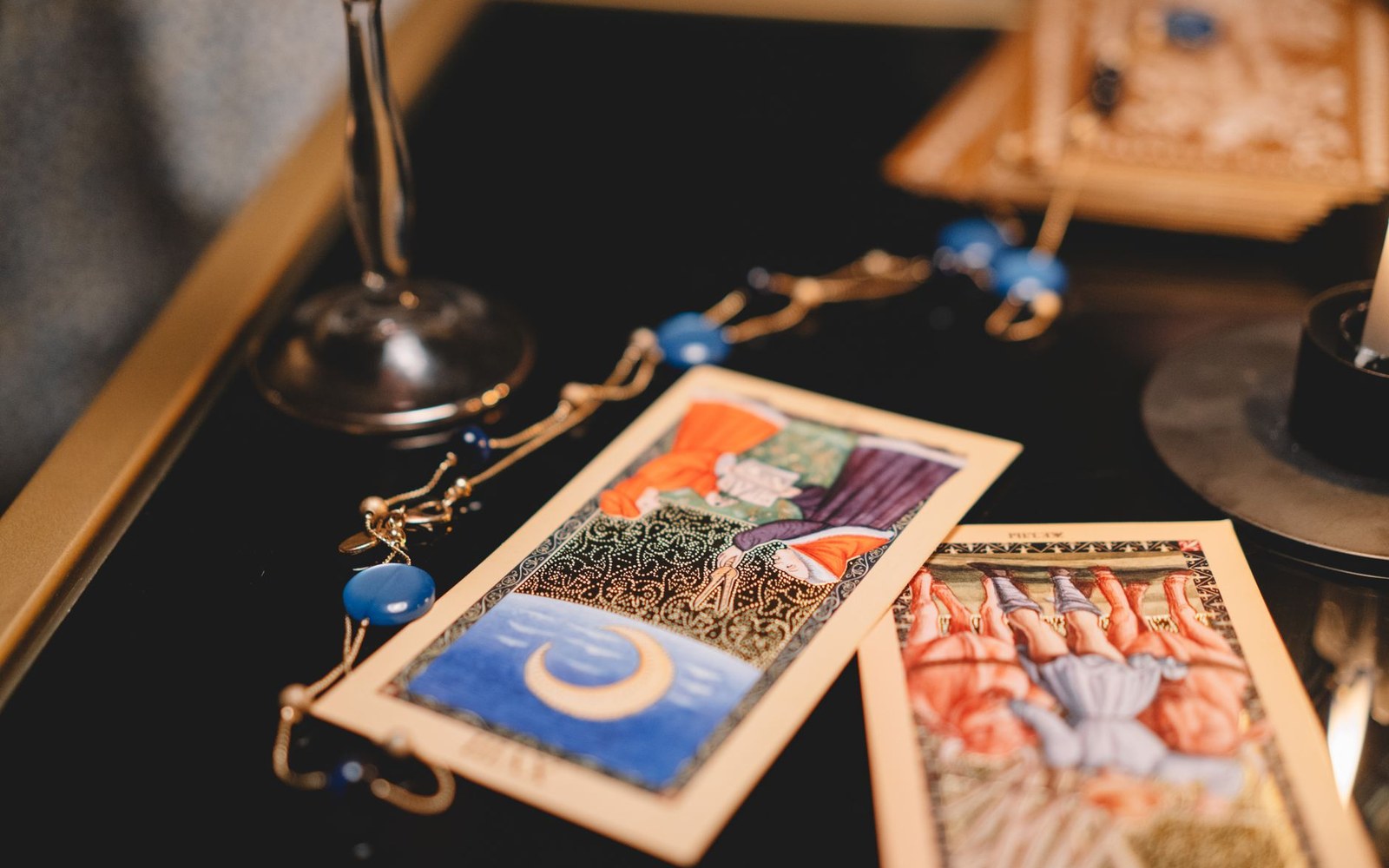 Illustrated tarot cards with a beaded chain and candle holder on a dark table