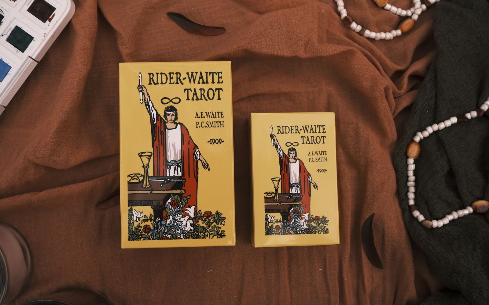 Two Rider-Waite Tarot deck boxes in different sizes on a brown fabric backdrop