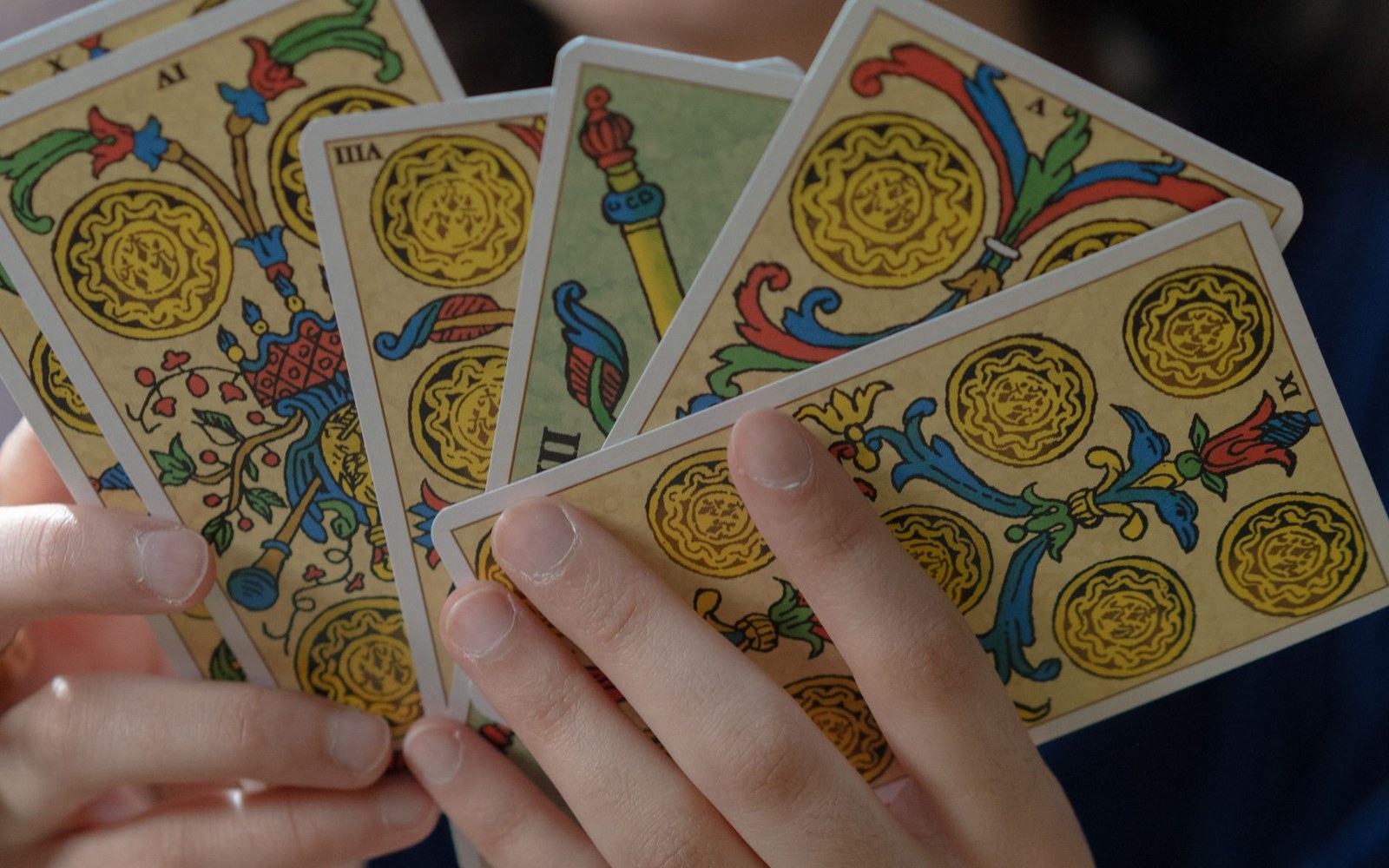 Hands fanning out a spread of ornately illustrated tarot cards with coin and staff suits