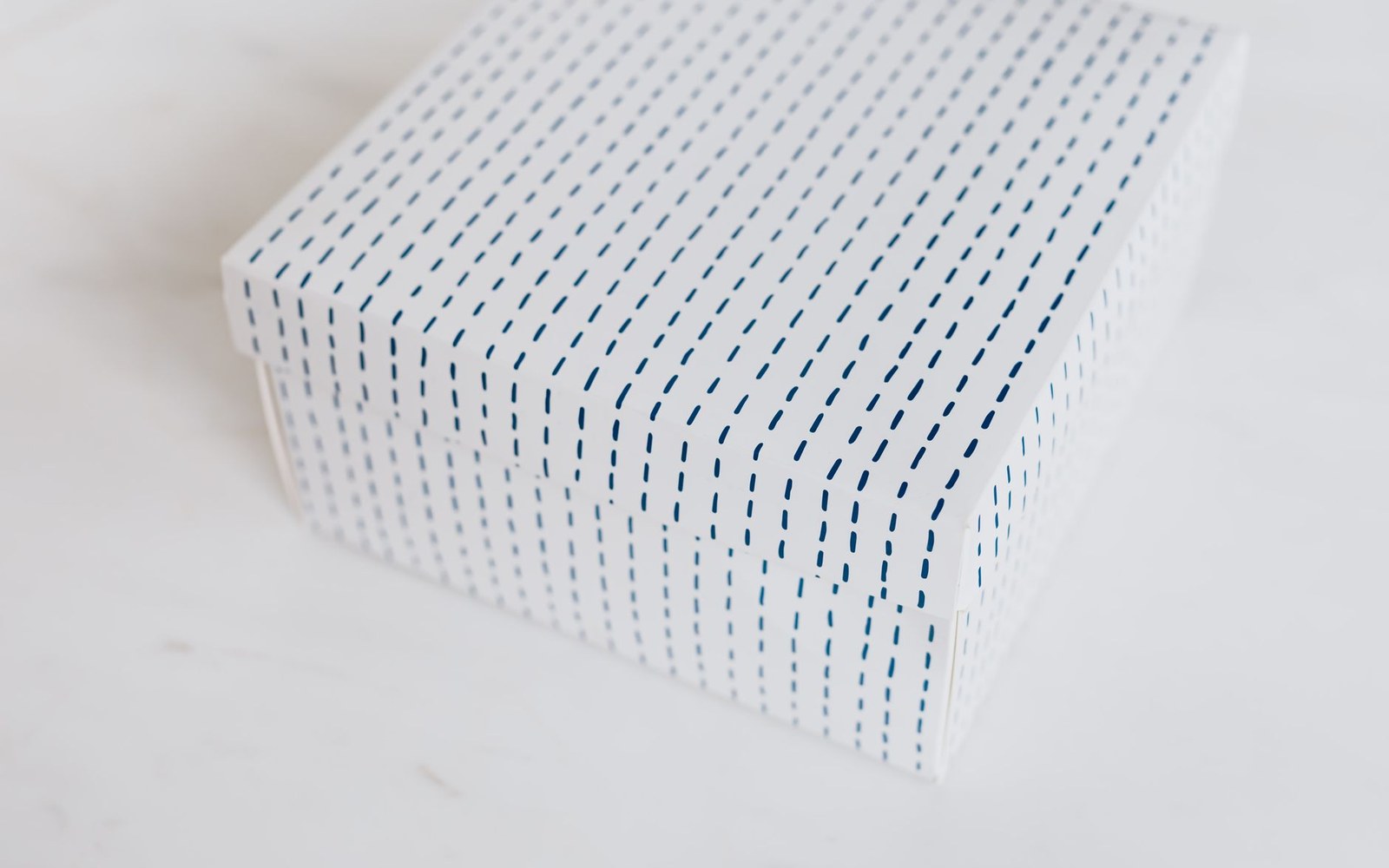 White gift box with blue dashed stripes sitting on a marble surface