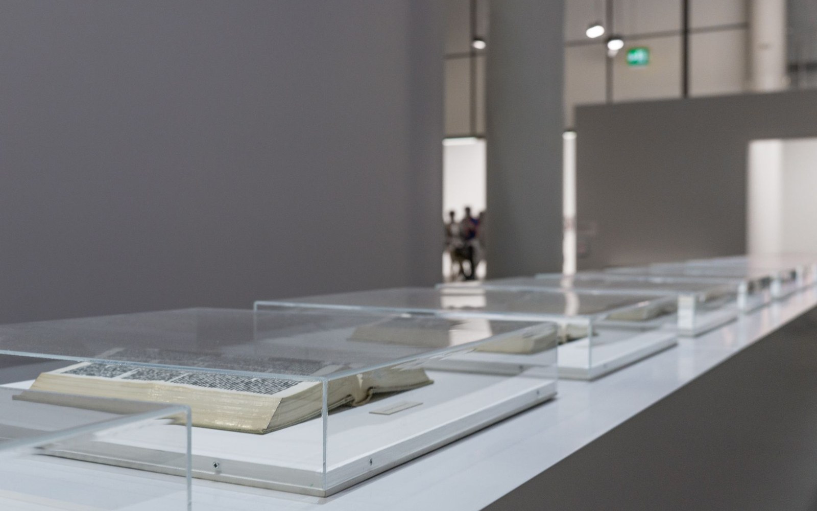 A museum display case containing a Visconti-Sforza card fragment under glass, an adult conservator visible in the background through the gallery room